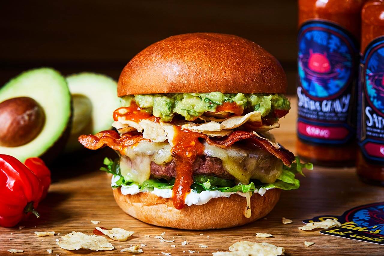 Honest beef burger with hot sauce, bacon, cheese, avocado and nachos